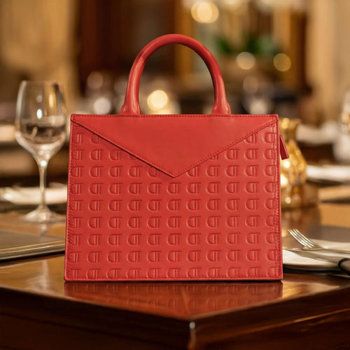Luxury Red Leather Envelope Bag resting on a table setting, displaying gold hardware details